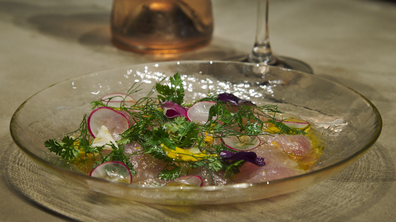 Red Sea Bream Carpaccio garnished with yuzu peel, herbs, and edible flowers on a plate